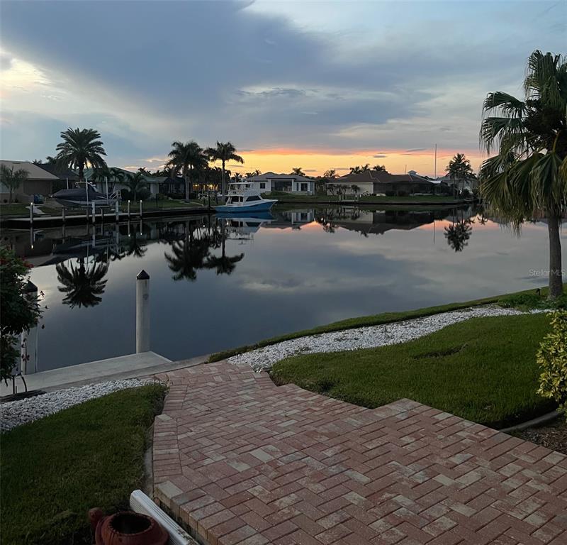 A brick patio overlooks a calm canal with boats, palm trees, and houses at sunset — 3433 NIGHTHAWK COURT, PUNTA GORDA, FL