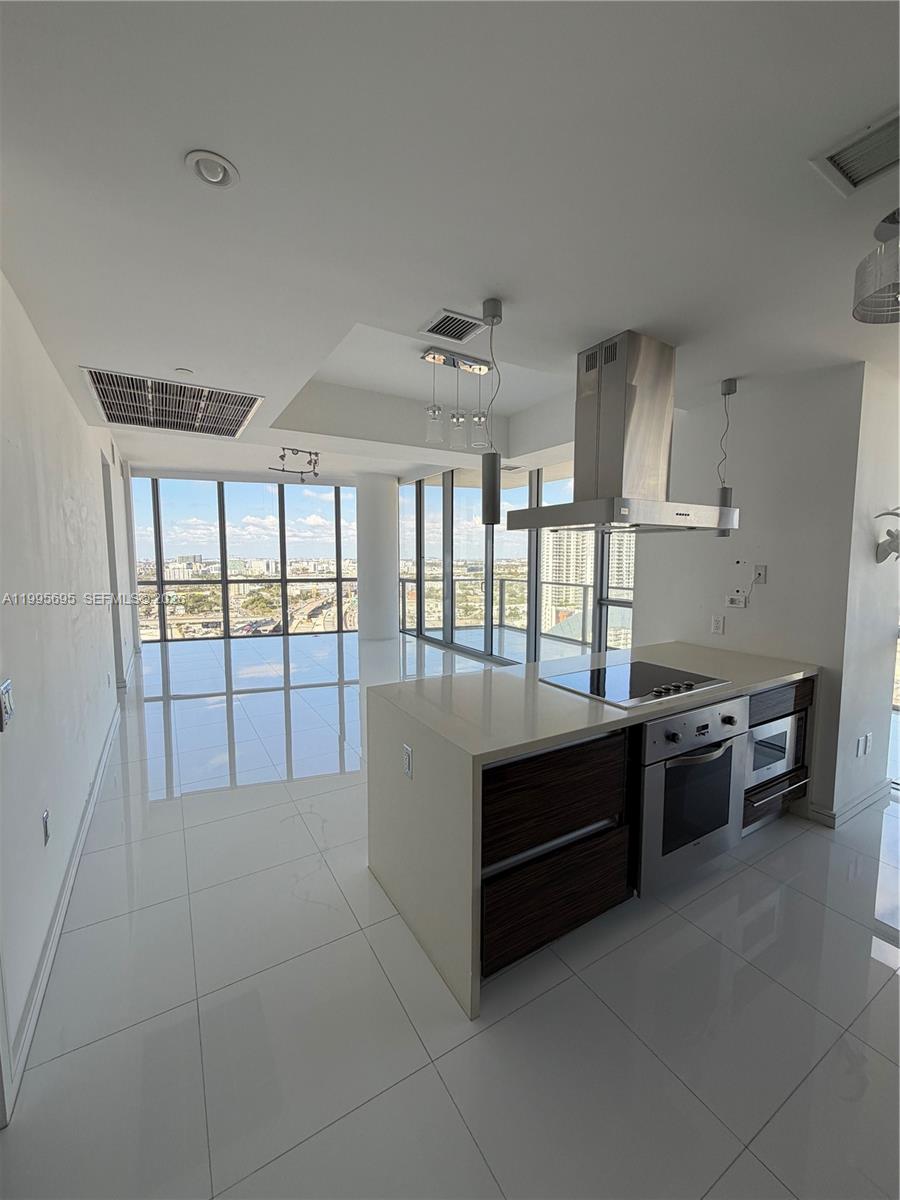 A modern kitchen with a central island and floor-to-ceiling windows overlooking a city skyline — 1100 Biscayne Blvd # 2605, Miami FL 33132, MIAMI, FL