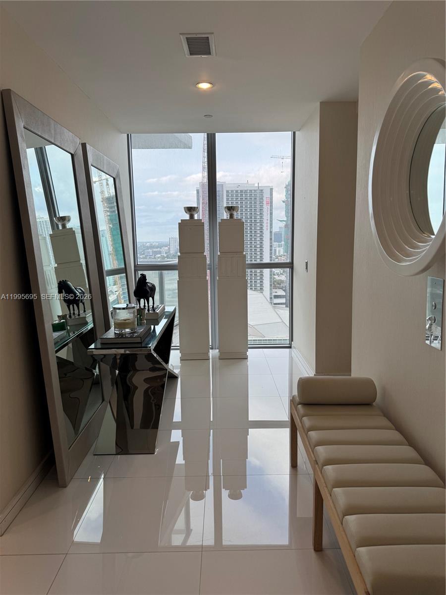 A modern hallway features white tile floors, a long bench, and floor-to-ceiling city views — 1100 Biscayne Blvd # 2605, Miami FL 33132, MIAMI, FL