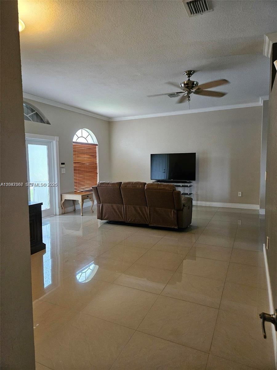 A living room features beige tile flooring, a brown leather sofa, and a ceiling fan — 2635 SE 4th Pl, Homestead FL 33033, HOMESTEAD, FL
