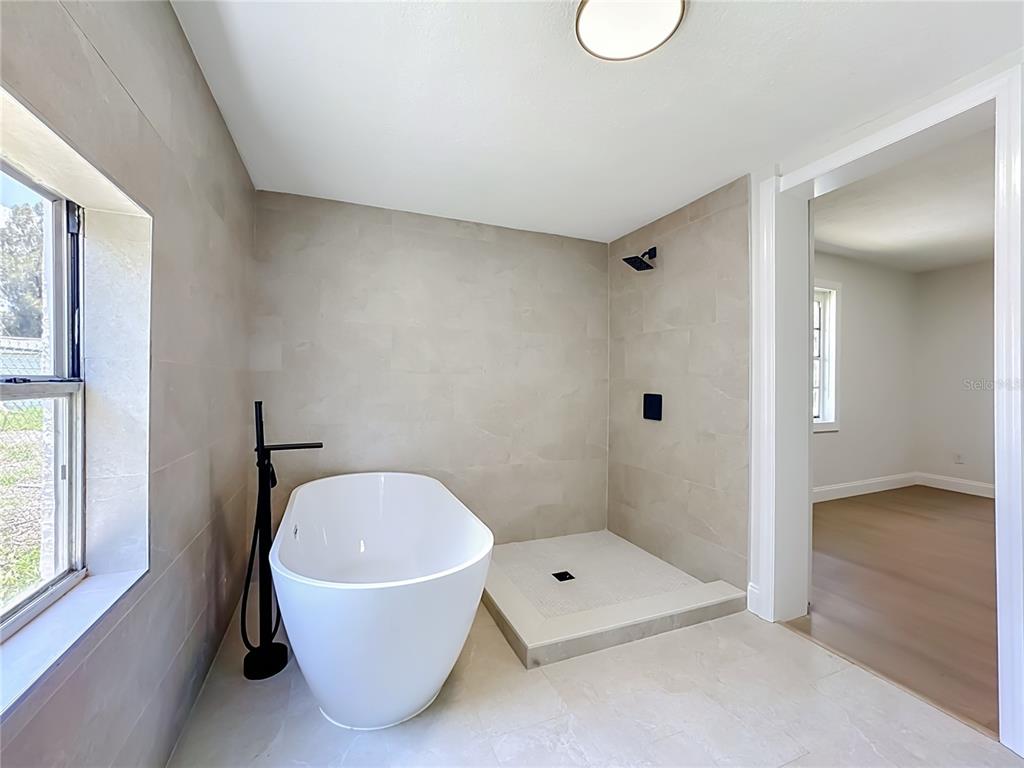 A bathroom features a freestanding white tub, a walk-in shower, and light-colored tile walls — 220 29TH STREET E, PALMETTO, FL