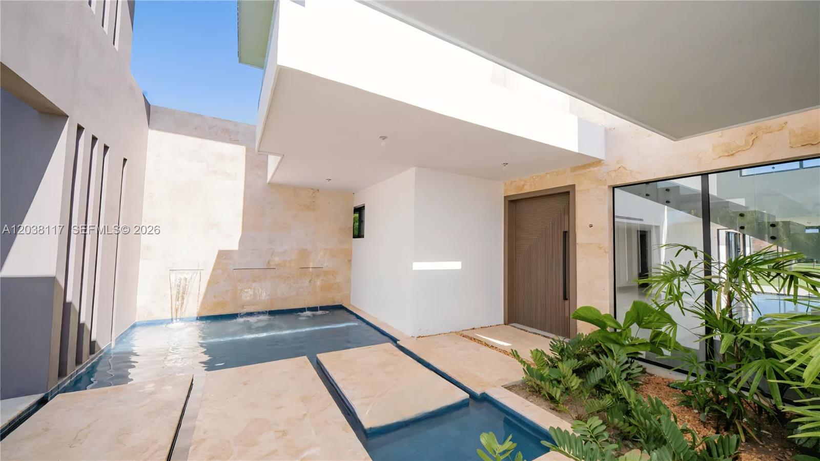 A modern home entrance features a reflecting pool, stone stepping stones, and a wooden door — 0 sv las palmas, FL