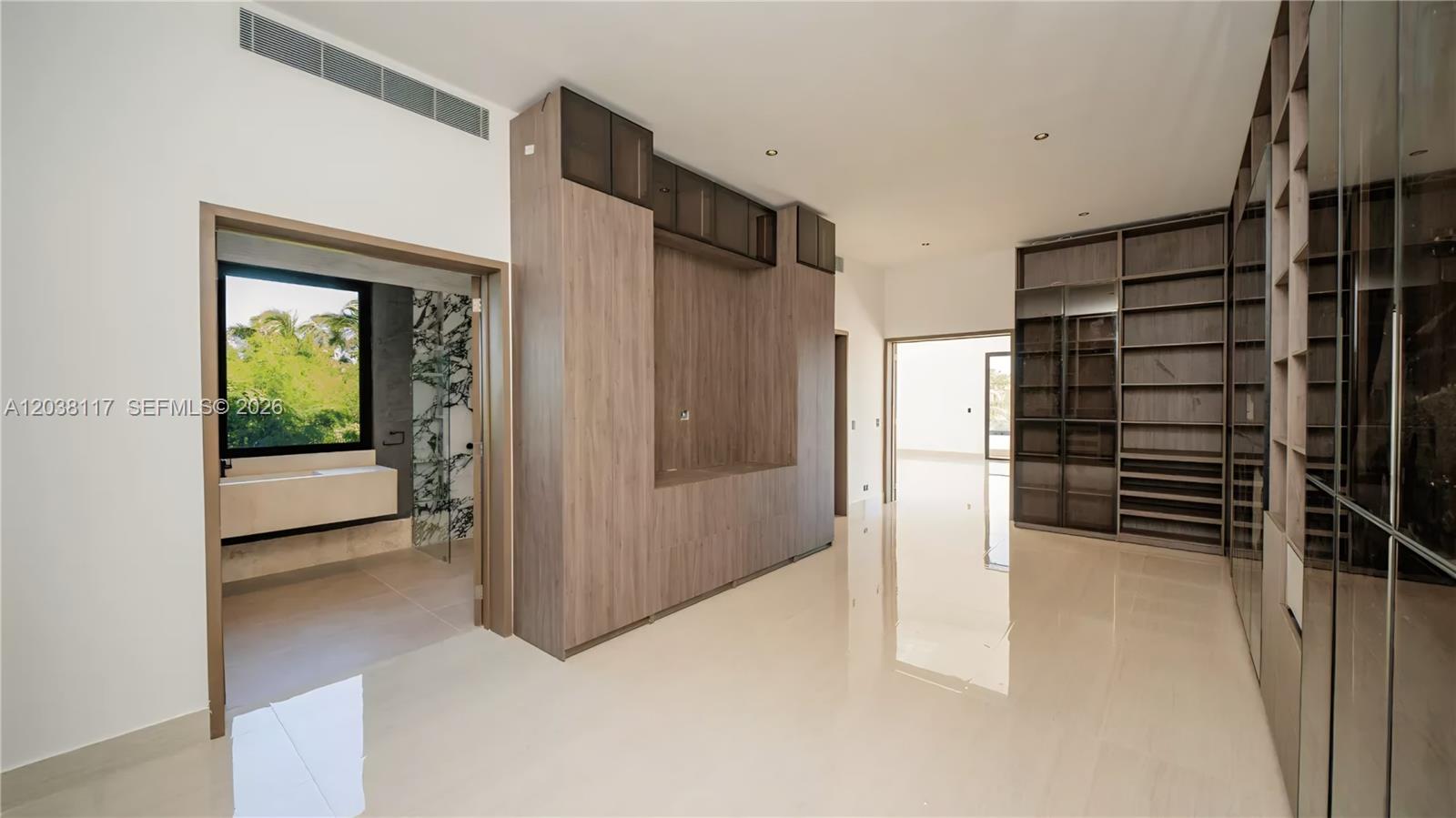 A modern walk-in closet features wood cabinetry, glass-front shelving, and an adjacent bathroom with greenery — 0 sv las palmas, FL