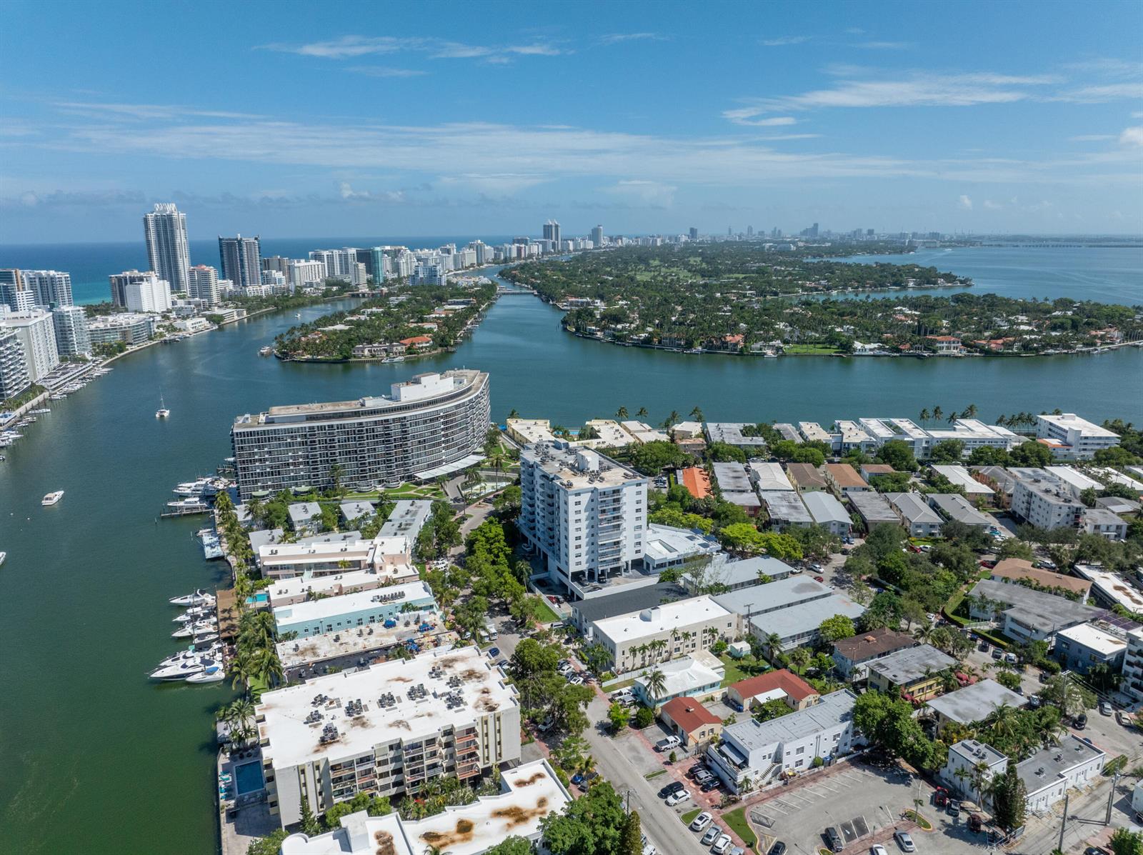 An aerial view shows a coastal neighborhood with apartment buildings, a waterway, and distant skyscrapers — 6900 Bay Drive # 11i, Miami Beach FL 33141, MIAMI BEACH, FL