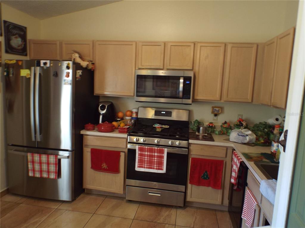 A kitchen features light wood cabinets, stainless steel appliances, and tiled flooring — 2546 SAGE DRIVE, KISSIMMEE, FL