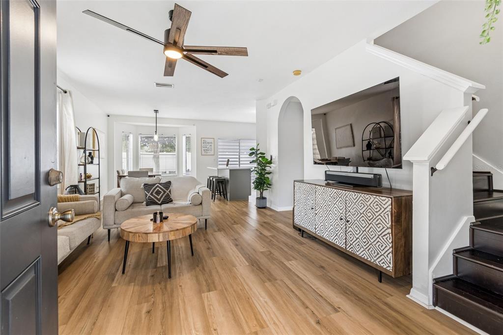 A bright living room features wood-look flooring, a ceiling fan, and a television above a cabinet — 12610 ADVENTURE DRIVE, RIVERVIEW, FL