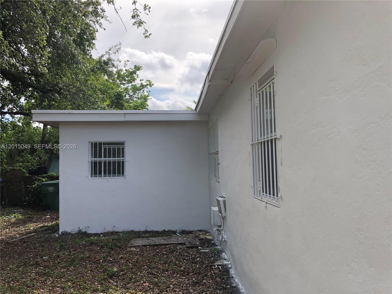 The exterior of a white stucco house features two windows with metal security bars — 166 NW 68th Ter, Miami FL 33150, MIAMI, FL