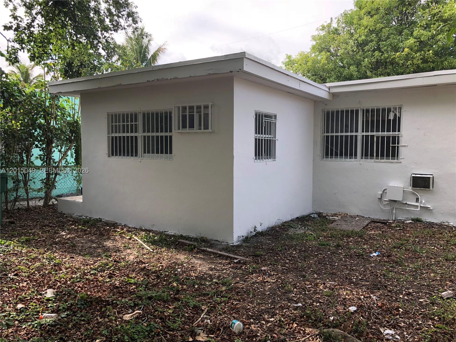 The exterior of a white, single-story house features barred windows and a flat roof — 166 NW 68th Ter, Miami FL 33150, MIAMI, FL