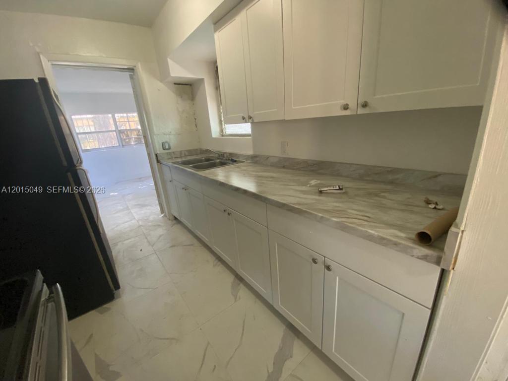 A kitchen features white cabinets, a marble-patterned countertop, and light-colored tile flooring — 166 NW 68th Ter, Miami FL 33150, MIAMI, FL