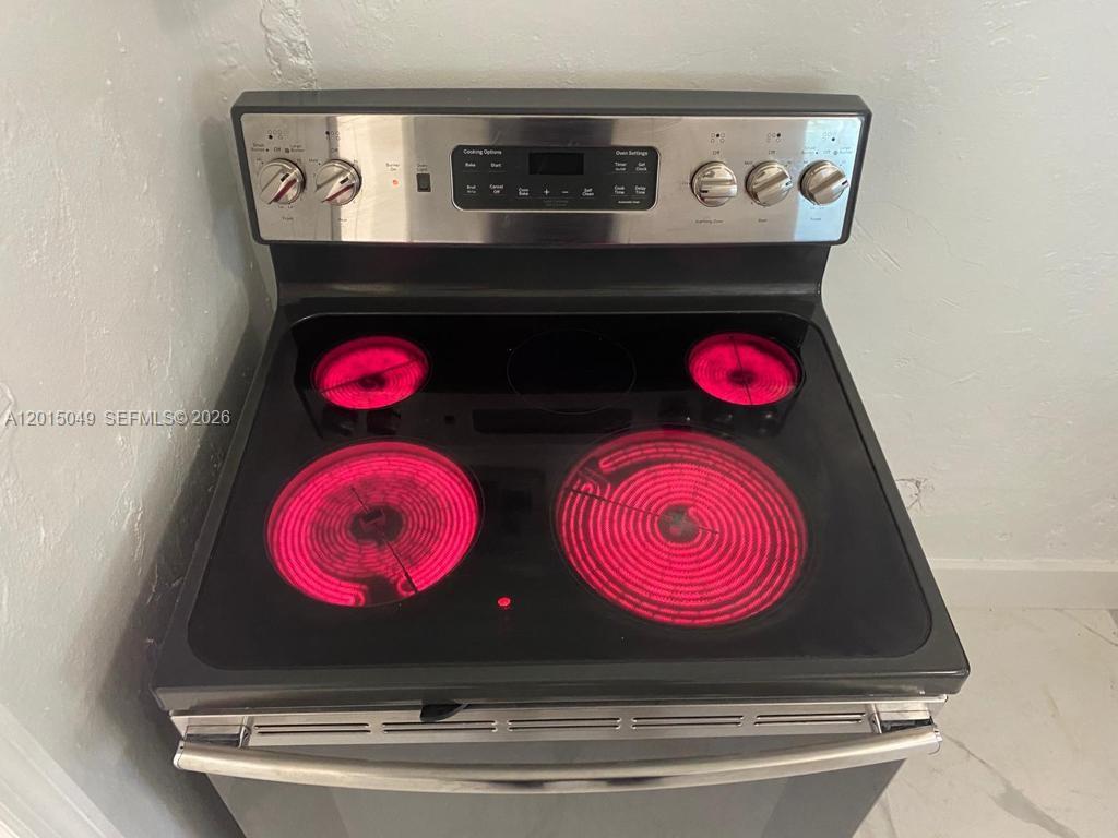 A stainless steel electric range with four active glowing burners sits against a white wall — 166 NW 68th Ter, Miami FL 33150, MIAMI, FL