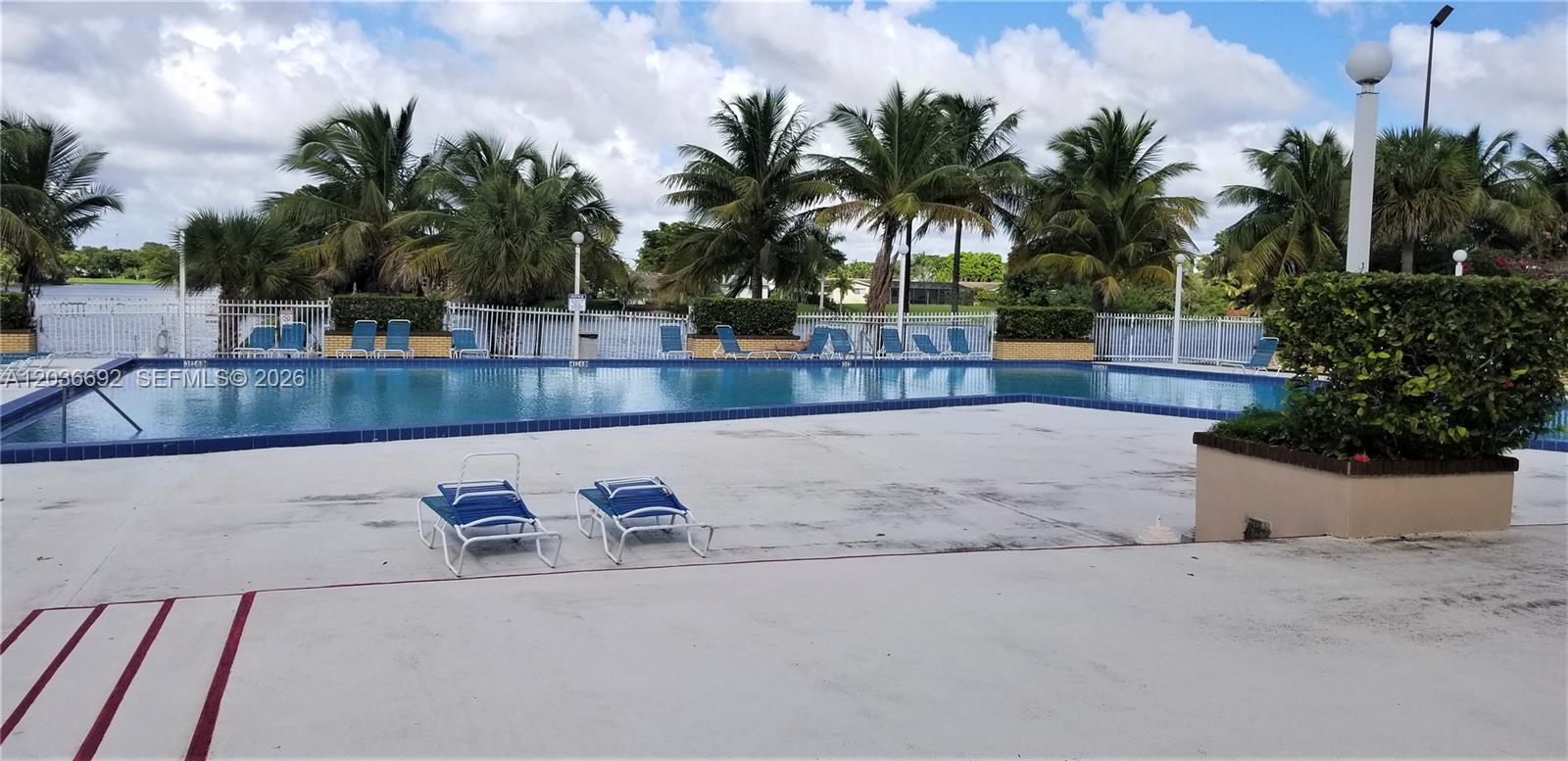 A swimming pool with lounge chairs sits on a patio surrounded by palm trees — 14201 N Kendall Dr # 405D, Miami FL 33186, MIAMI, FL