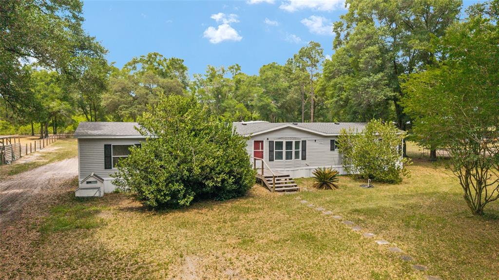 A single-story manufactured home with gray siding sits on a grassy lot with mature trees — 19551 SE 42ND PLACE, MORRISTON, FL