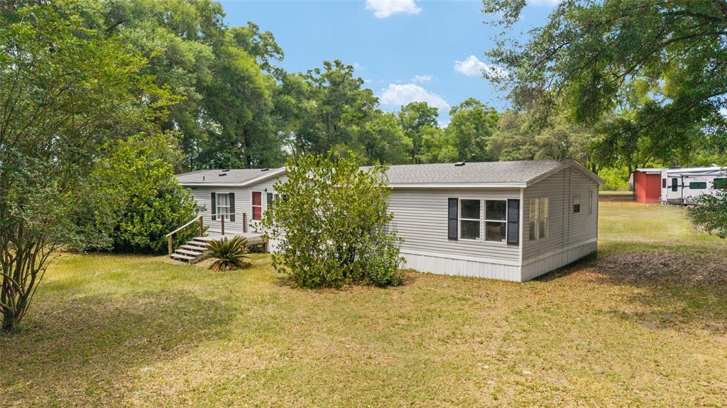 A single-story manufactured home with light gray siding sits on a grassy, tree-lined lot — 19551 SE 42ND PLACE, MORRISTON, FL