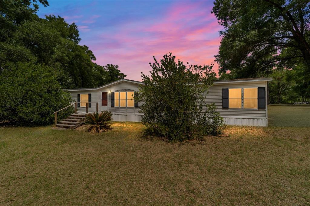 A single-story manufactured home with light siding sits on a grassy lot at sunset — 19551 SE 42ND PLACE, MORRISTON, FL