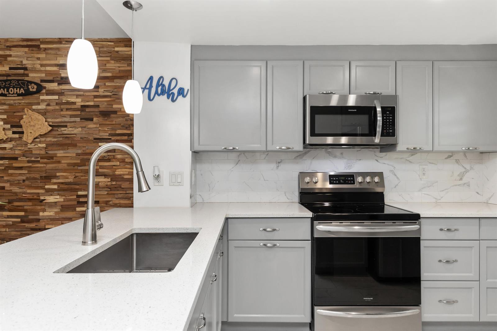 A kitchen features gray cabinets, white quartz countertops, a marble backsplash, and a wood-paneled wall — 9780 Marina Boulevard # 421, Boca Raton FL 33428, BOCA RATON, FL