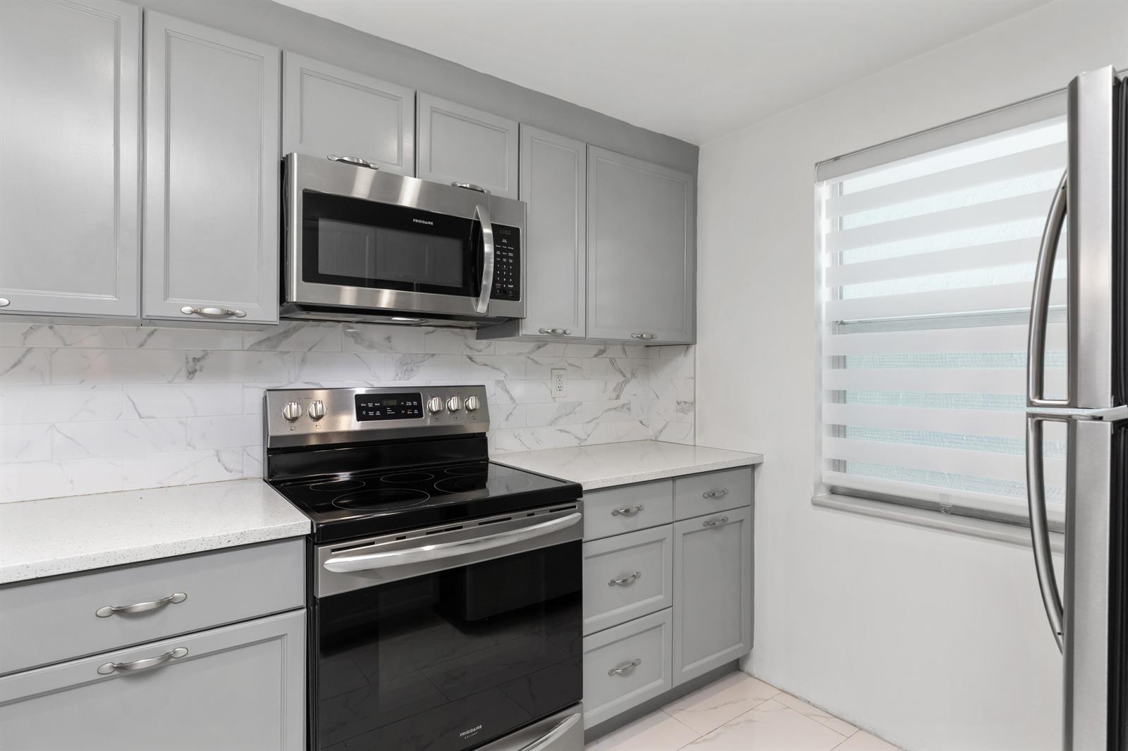 A kitchen featuring gray cabinets, stainless steel appliances, white countertops, and marble-style backsplash tiles — 9780 Marina Boulevard # 421, Boca Raton FL 33428, BOCA RATON, FL
