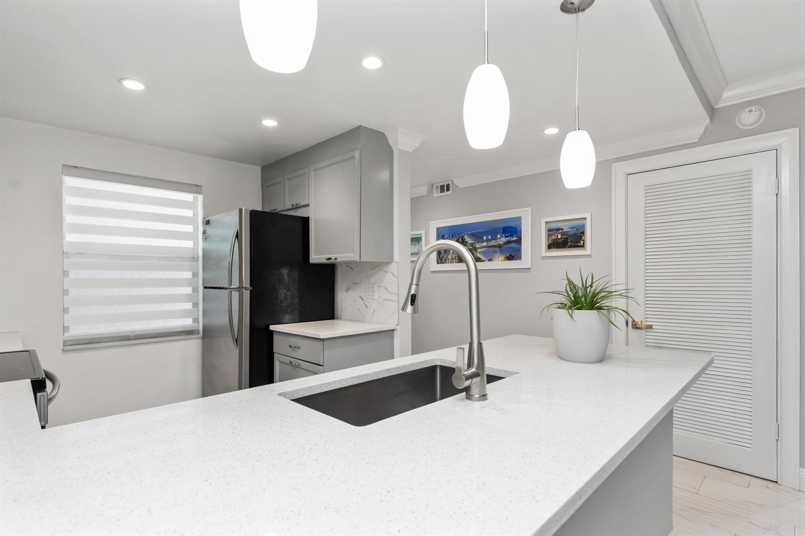 A modern kitchen features a white quartz island, gray cabinetry, and stainless steel appliances — 9780 Marina Boulevard # 421, Boca Raton FL 33428, BOCA RATON, FL