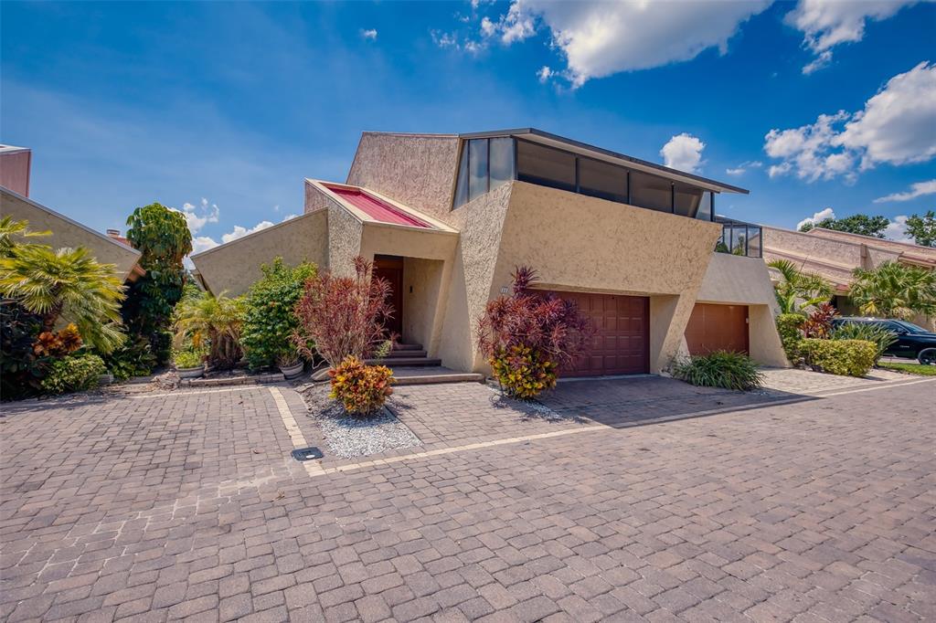A modern house with a textured beige exterior, angular rooflines, and a brick-paved driveway — 11 CASARENA COURT, WINTER HAVEN, FL