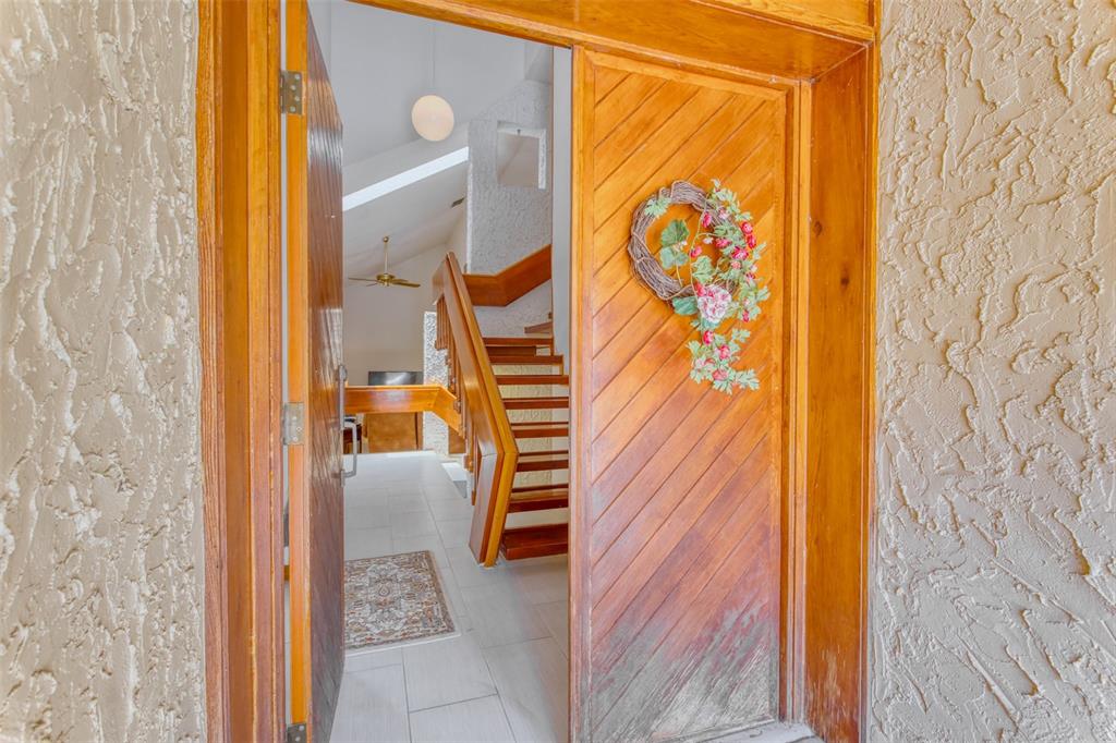 An open wooden front door reveals a tiled entryway with a staircase and vaulted ceiling — 11 CASARENA COURT, WINTER HAVEN, FL