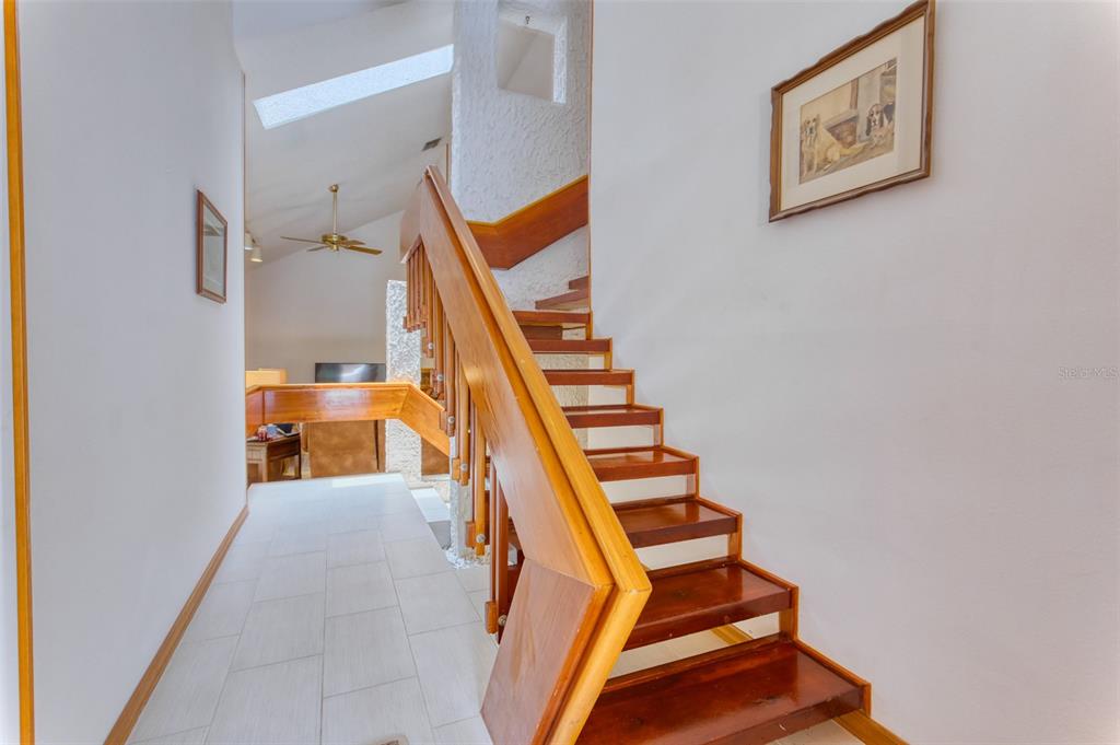 A wooden staircase with open risers leads upward in a hallway with white tiled floors — 11 CASARENA COURT, WINTER HAVEN, FL