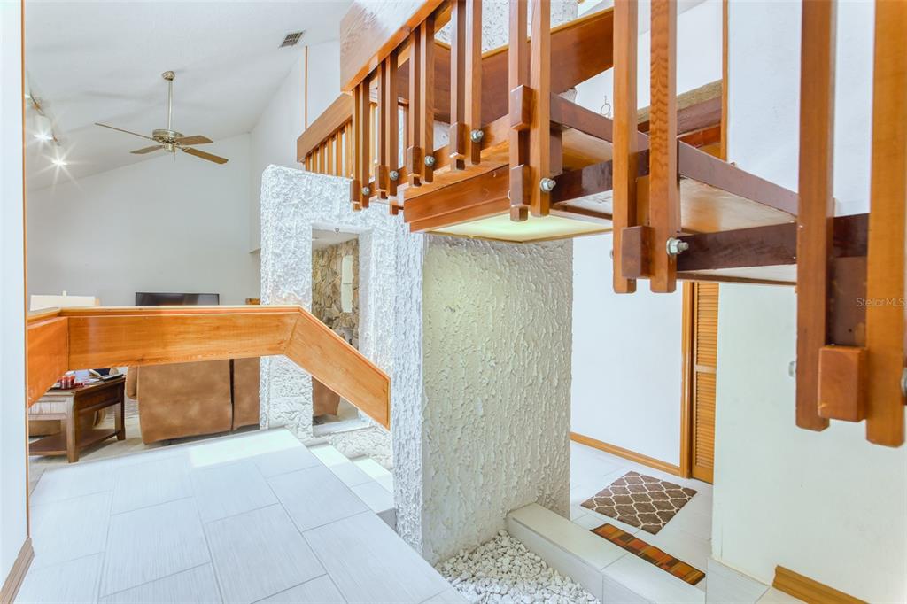 A wooden staircase with a railing overlooks a tiled entryway with a white stone floor — 11 CASARENA COURT, WINTER HAVEN, FL
