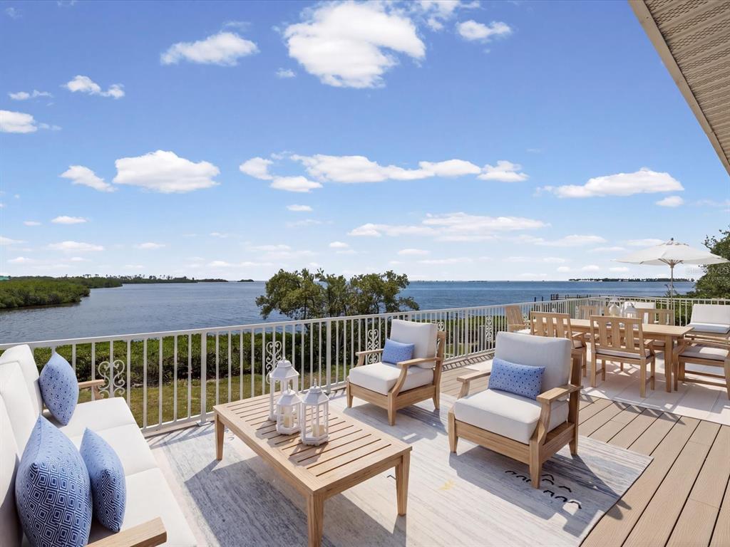 A wooden deck features outdoor seating, a coffee table, and a railing overlooking the water — 1647 SEA BREEZE DRIVE, TARPON SPRINGS, FL