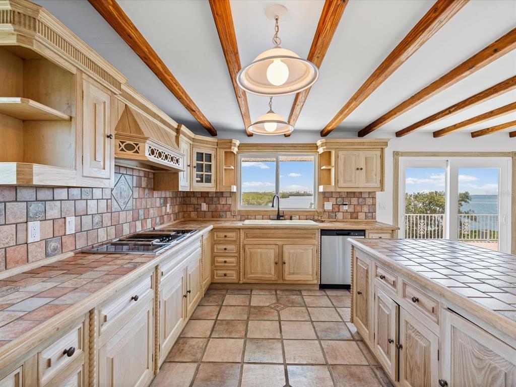 A kitchen with wood cabinets, tile countertops, exposed ceiling beams, and a view of water — 1647 SEA BREEZE DRIVE, TARPON SPRINGS, FL