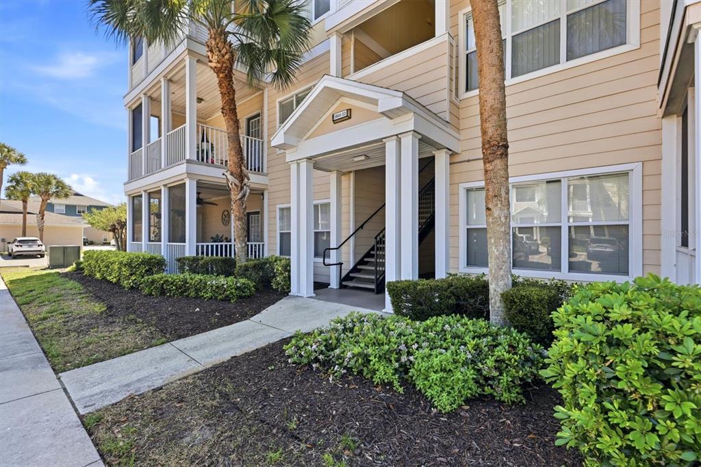 The exterior of a multi-story apartment building features a covered entrance with stairs and landscaping — 4802 51ST STREET W UNIT 1801, BRADENTON, FL