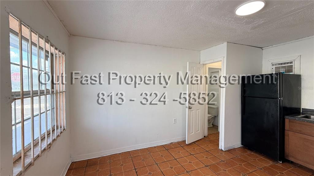 A kitchen with tiled floors, a black refrigerator, and a window with security bars — 9718 N NEBRASKA AVENUE UNIT 3, TAMPA, FL