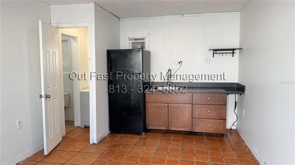A kitchen area features a black refrigerator, wooden cabinets, a sink, and tiled flooring — 9718 N NEBRASKA AVENUE UNIT 3, TAMPA, FL