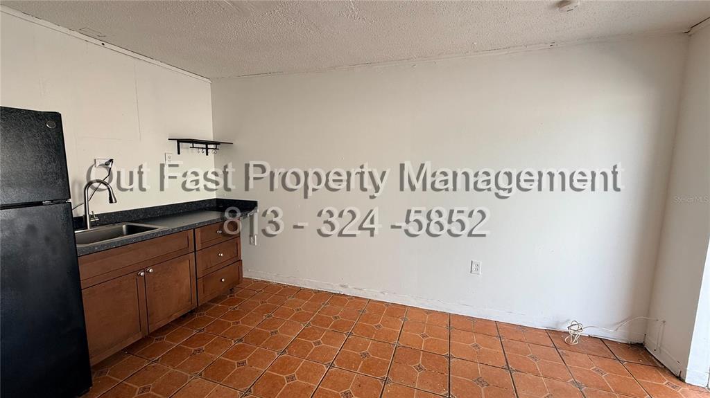 A small kitchen features brown cabinets, a black refrigerator, and orange tile flooring — 9718 N NEBRASKA AVENUE UNIT 3, TAMPA, FL