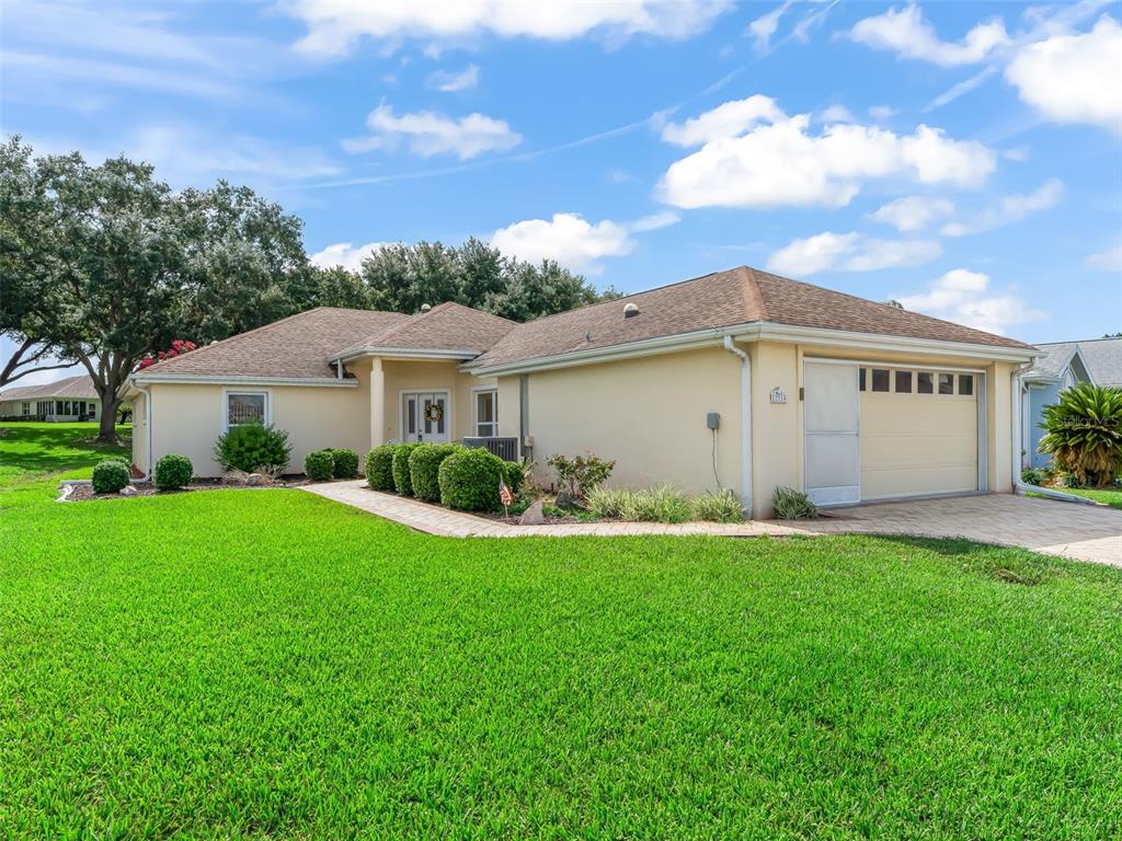 A single-story house with a beige stucco exterior, a two-car garage, and a green lawn — 17719 SE 114TH COURT, SUMMERFIELD, FL