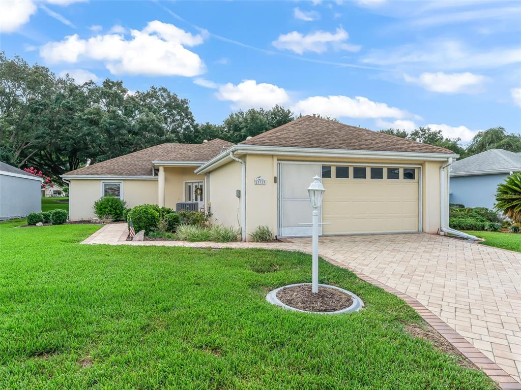 A single-story house with a beige stucco exterior, a tan shingle roof, and a paved driveway — 17719 SE 114TH COURT, SUMMERFIELD, FL