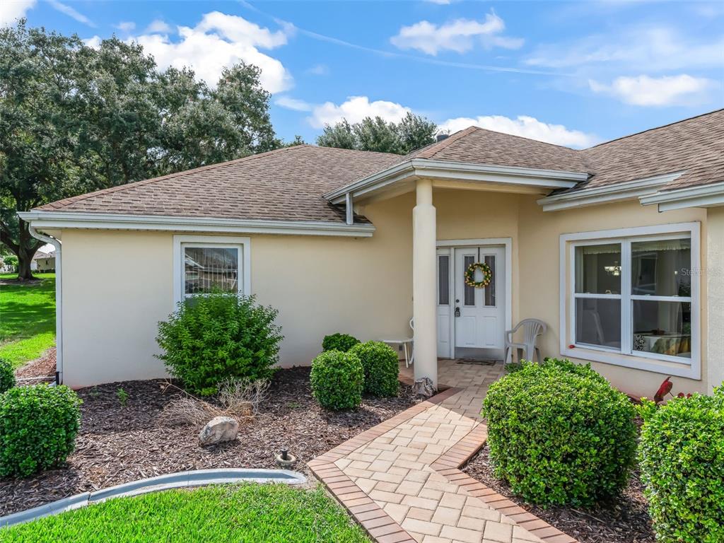 The exterior of a single-story house features a paved walkway leading to a white front door — 17719 SE 114TH COURT, SUMMERFIELD, FL