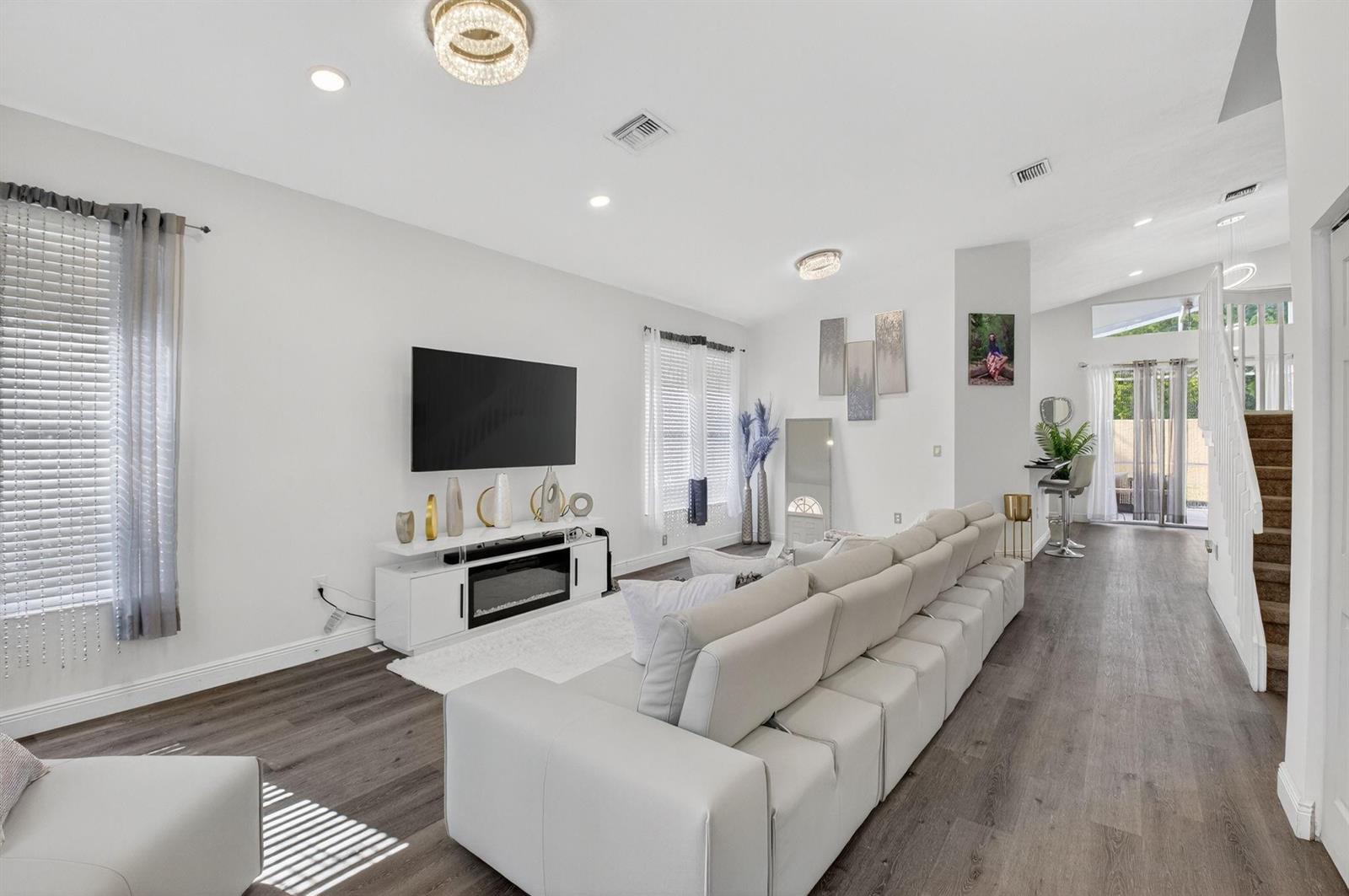 A bright living room features a large sectional sofa, wall-mounted television, and wood-look flooring — 1023 Fairfax Circle, Boynton Beach FL 33436, BOYNTON BEACH, FL