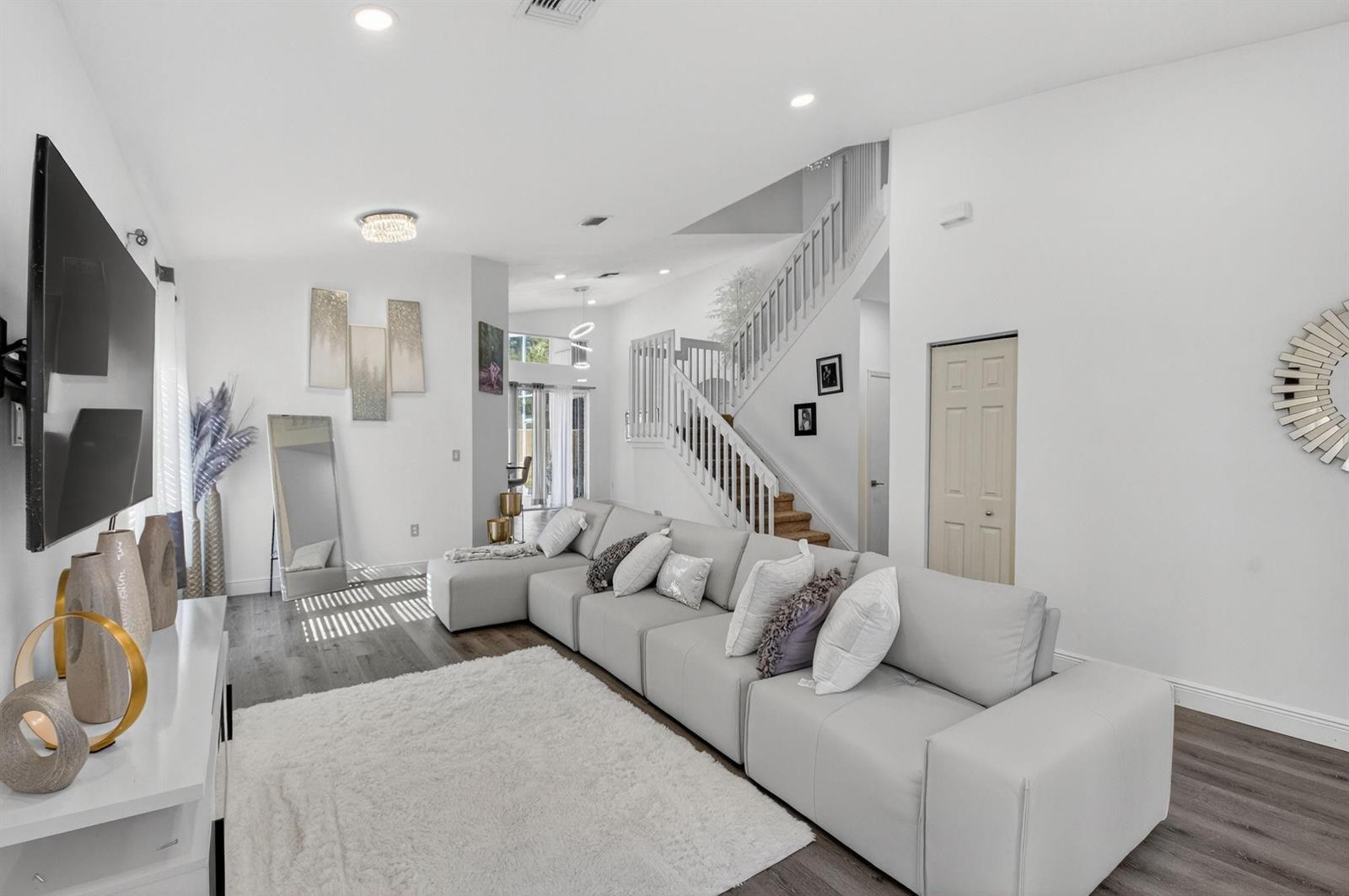 A modern living room features a large sectional sofa, white walls, and a staircase — 1023 Fairfax Circle, Boynton Beach FL 33436, BOYNTON BEACH, FL