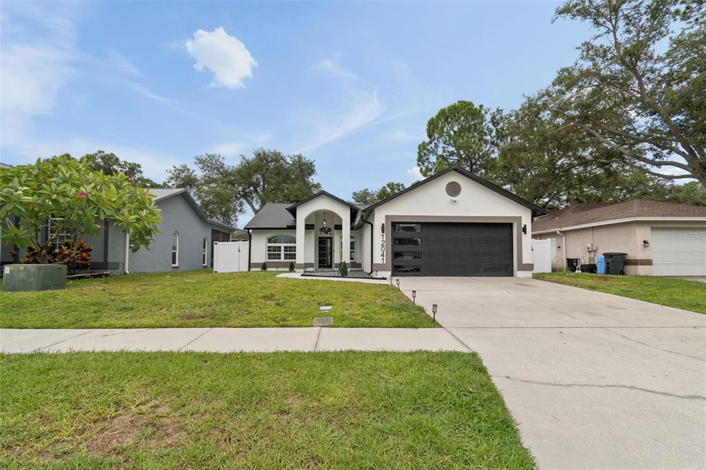 A single-story house with a white exterior, black garage door, and arched entryway — 12041 68TH STREET, LARGO, FL