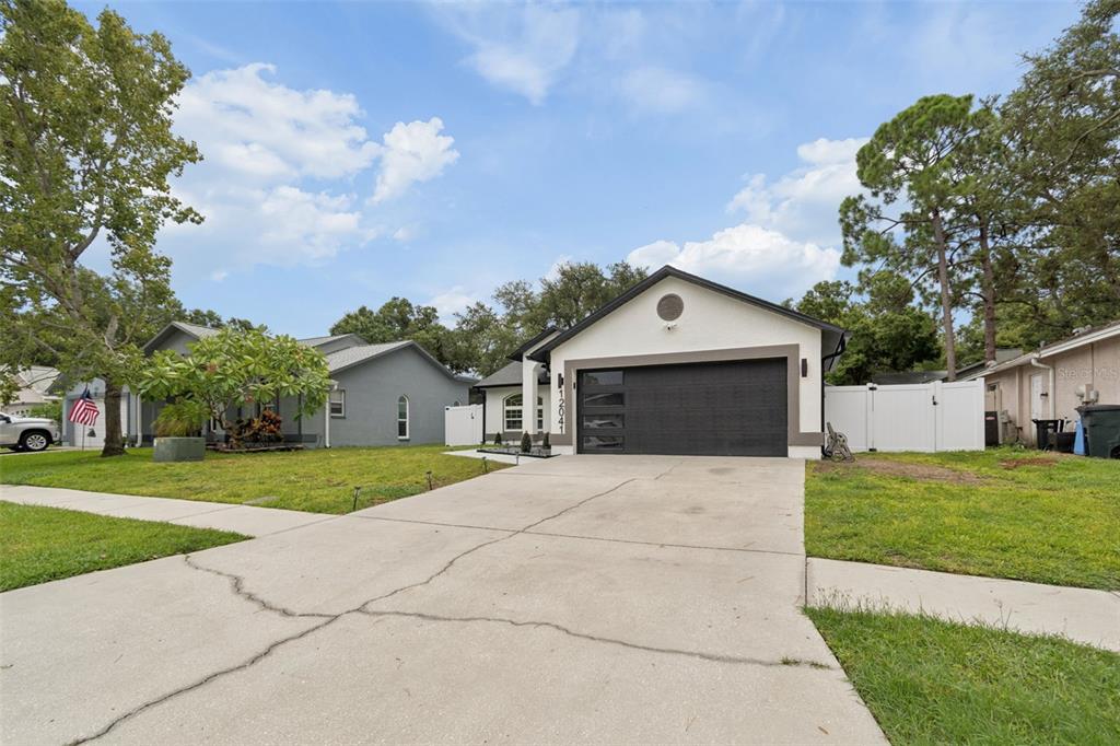 A single-story house with a black garage door and a concrete driveway under a blue sky — 12041 68TH STREET, LARGO, FL