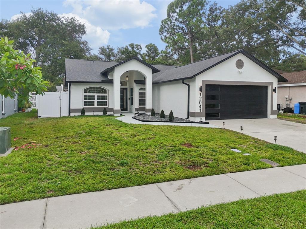 A single-story house with a white stucco exterior, black trim, and a two-car garage — 12041 68TH STREET, LARGO, FL