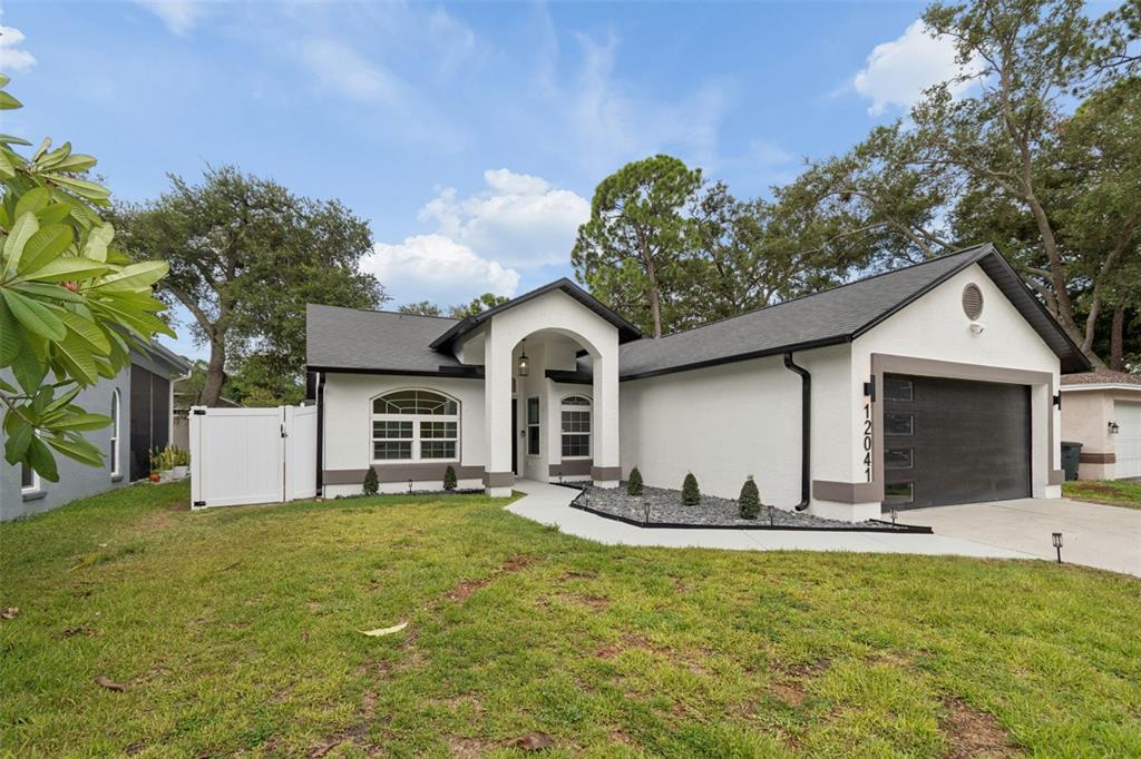 A single-story house with a white stucco exterior, dark trim, and a two-car garage — 12041 68TH STREET, LARGO, FL