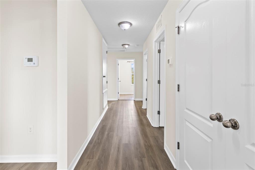 A hallway with wood-look flooring leads to a doorway at the end of the corridor — 12210 MOSS LAKE LOOP, NEW PORT RICHEY, FL