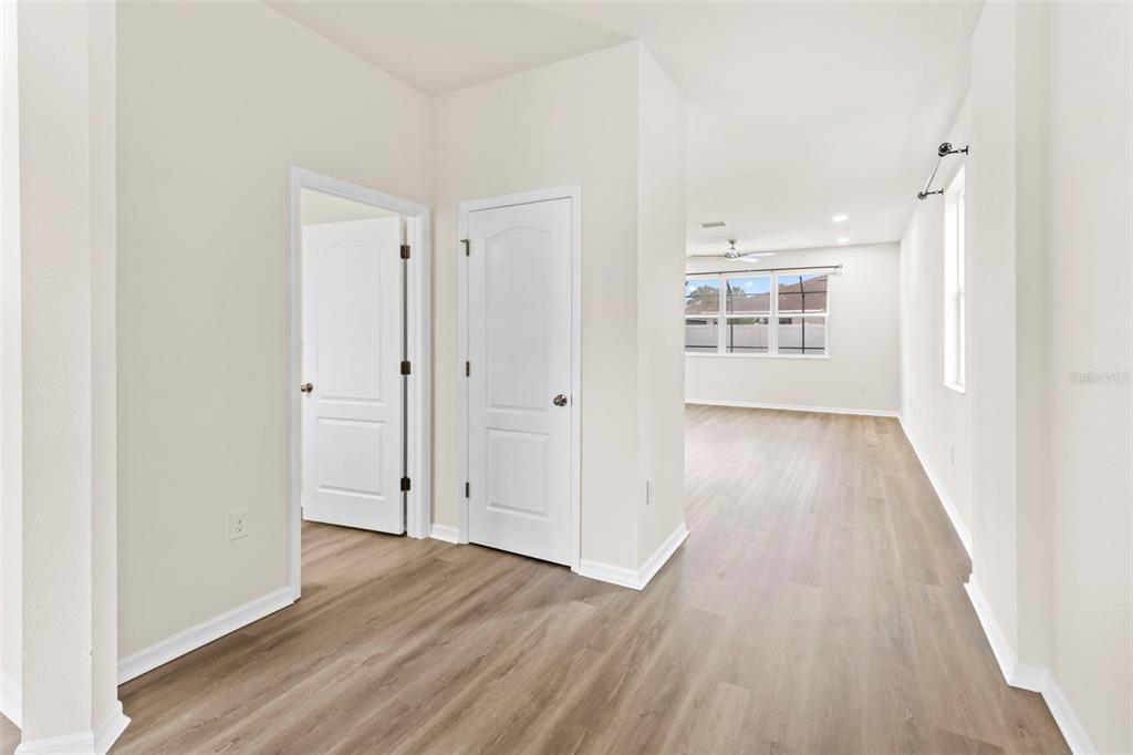 A hallway with light wood-look flooring leads to an open living area with large windows — 12210 MOSS LAKE LOOP, NEW PORT RICHEY, FL