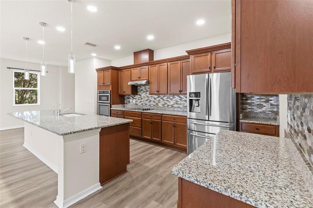 A kitchen features wood cabinets, granite countertops, a large island, and stainless steel appliances — 12210 MOSS LAKE LOOP, NEW PORT RICHEY, FL
