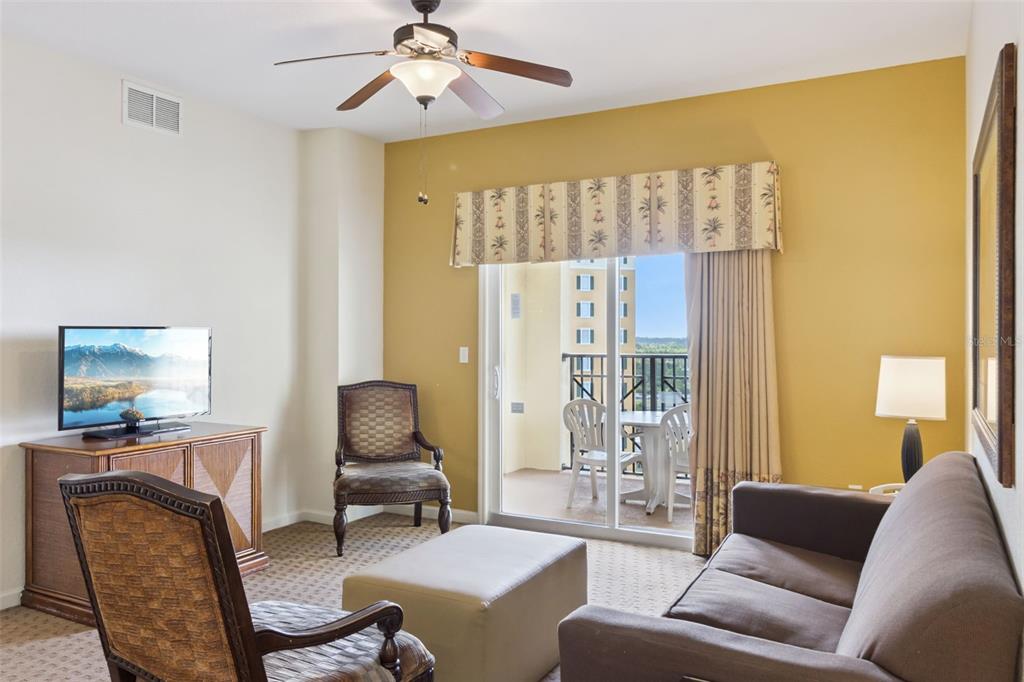 A living room features a sofa, armchairs, a television, and a sliding door to a balcony — 8101 RESORT VILLAGE DRIVE UNIT 31110, ORLANDO, FL