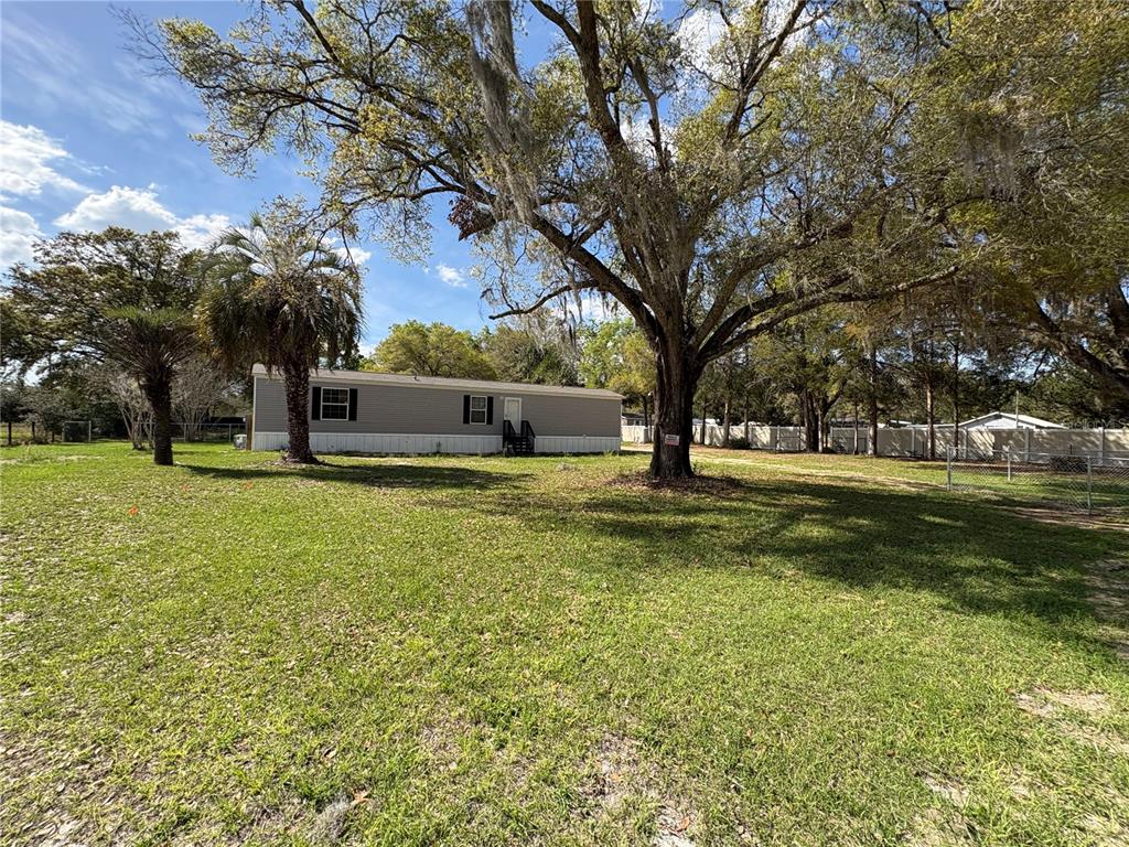 A single-story manufactured home sits on a grassy lot shaded by large oak trees — 238 NW 76TH TERRACE, OCALA, FL