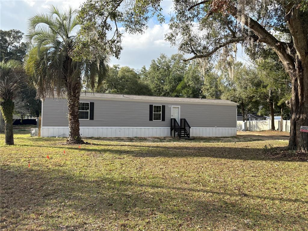 A gray manufactured home sits on a grassy lot with a palm tree and trees — 238 NW 76TH TERRACE, OCALA, FL