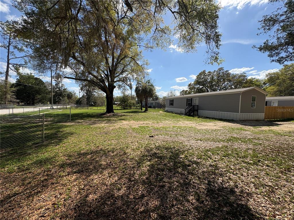A mobile home sits on a large, grassy lot with mature trees and a chain-link fence — 238 NW 76TH TERRACE, OCALA, FL