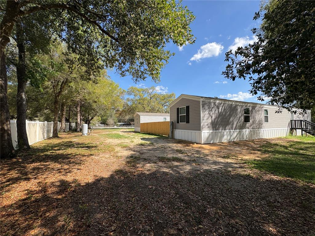 A view of a mobile home exterior with a fenced yard and surrounding trees — 238 NW 76TH TERRACE, OCALA, FL
