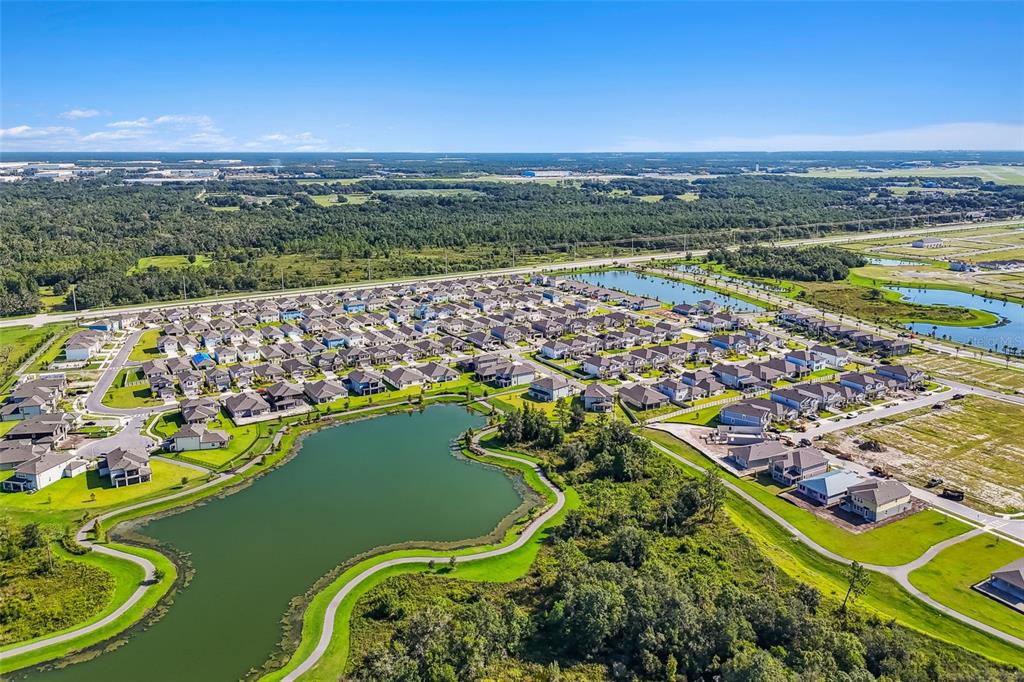 An aerial view shows a suburban neighborhood with many houses surrounding a large retention pond — 5571 FREESIA DRIVE, LAKELAND, FL
