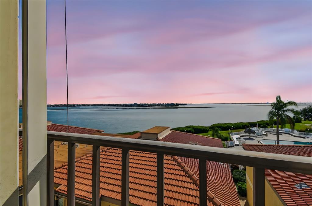 A balcony overlooks a swimming pool, red-tiled roofs, and a calm bay at sunset — 6104 PALMA DEL MAR BOULEVARD S UNIT 402, ST PETERSBURG, FL